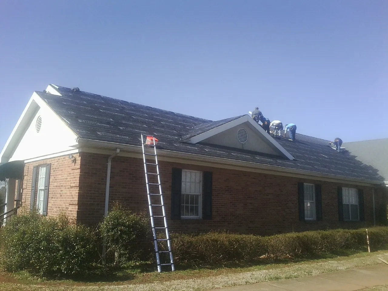 Crew tearing shingles off a brick ranch roof with a ladder set — Emergency Roof Repair work by our crew in South Gate