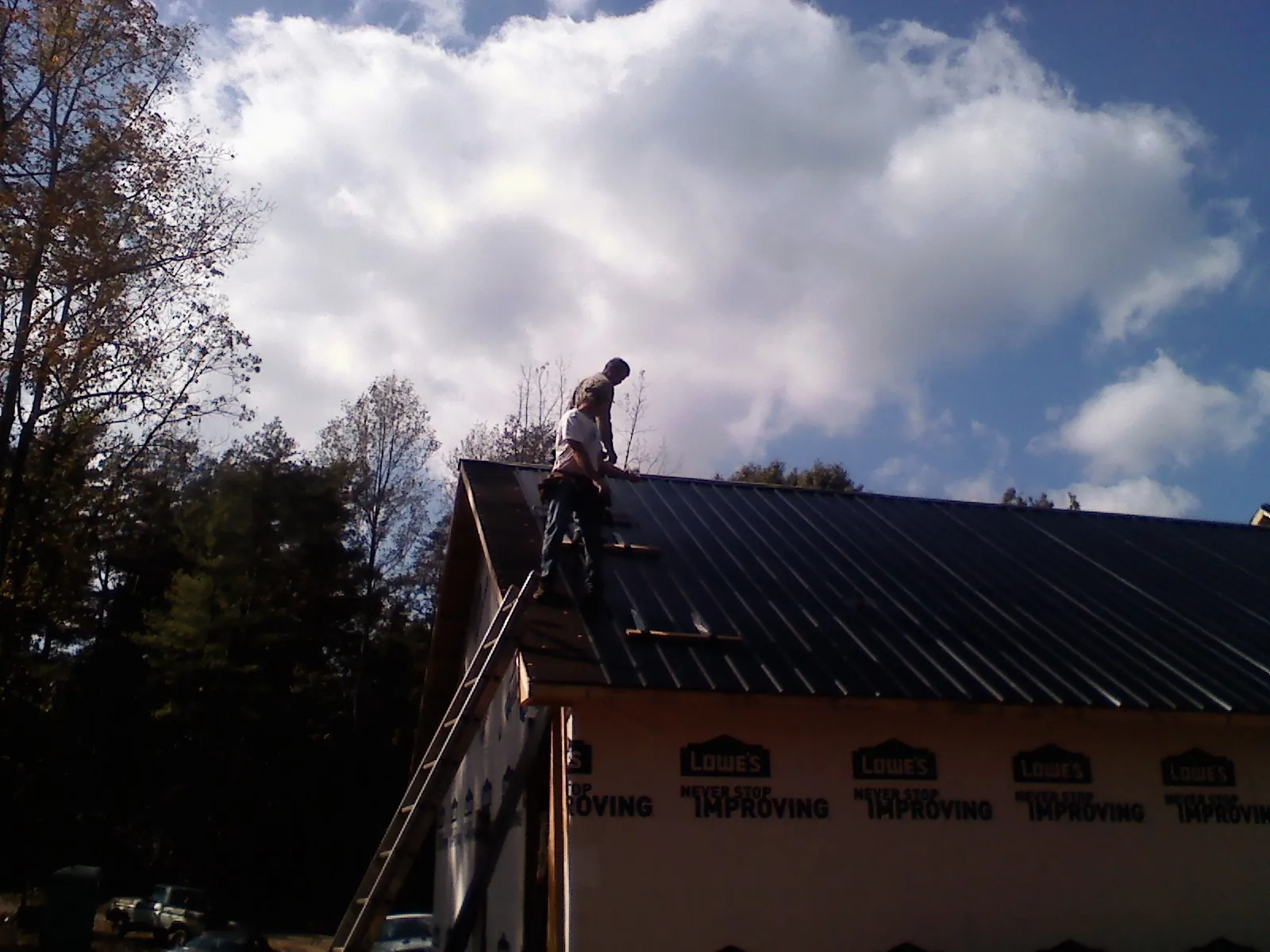 Roofer fastening dark metal panels high against a cloudy sky, from a Roof Inspection job in South Gate
